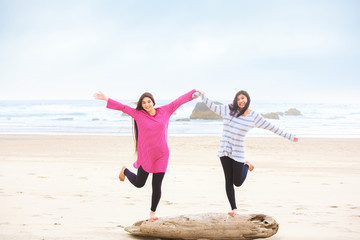 Two teen girls balancing on log at beach