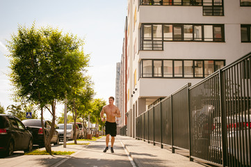 Handsome sexy male bodybuilder athlete man with naked torso, Morning run in open air in urban courtyards, early sunny summer morning. Healthy lifestyle concept.
