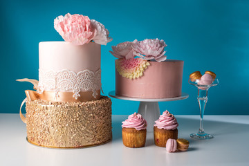 Luxury wedding table with a beautiful pink cake decorated with mastic pink rose and gold on a blue...
