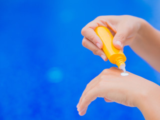 Woman hand apply sunscreen / sunblock by the swimming pool. Vacation and relaxation, summer travel concept.