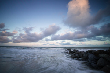 storm jetty made of rocks and a rising tide and ocean at dawn with a cloudy sky at sunrise
