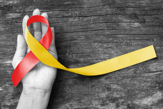 World hepatitis day and HIV/ HCV co-infection awareness with red yellow ribbon  (isolated  with clipping path) on person's hand support and old aged wood