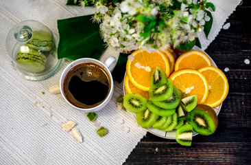 Morning tea or coffee with orange and kiwies slices and green macaroons on a white blanket with cherry blossom
