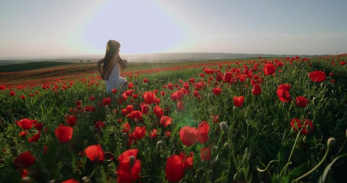 little Asian girl in white dress fun runs in field of red poppies on a Sunny spring day in slow motion