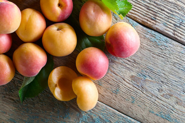 Juicy fresh apricots with leaves on old wooden table .