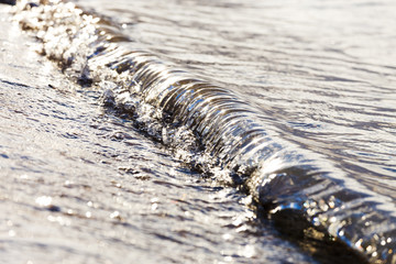 A small wave crashes on the beach in metallic morning light.