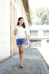 Young beautiful woman walking with mobile phone and headphones. Summer.