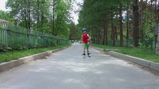 Young boy roller skating on the road in suburbs in summer day. His younger brother is riding him on a bicycle.