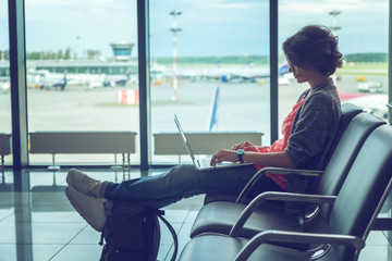 Young beautiful woman traveler sits at the airport with a laptop while waiting for her flight