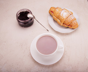 Croissant with raspberry jam, on the table a mobile phone and cocoa in a mug.