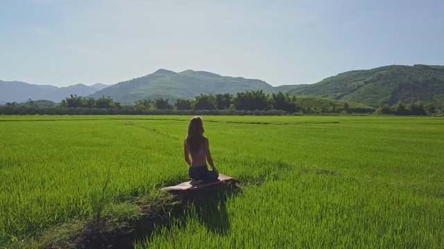 Flycam Removes from Blond Girl Sitting on Mat among Landscape