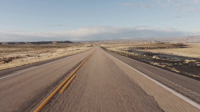 Driving USA: Spectacular point of view car shot speeding across desert grasslands at sunrise or sunset, Wyoming
