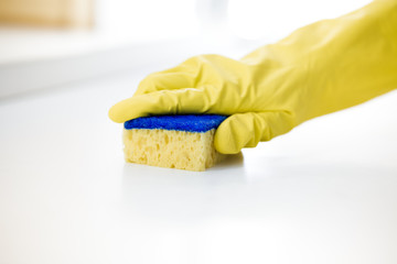 Female hand in rubber yellow glove cleans surface of table