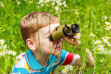 A five-year-old boy with red hair plays: sitting in an ambush on a flowering meadow looking at toy...