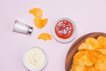 Concept of unhealthy food. Cheese and onion potato chips with hot chilli sauce on pink background.