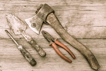 Old stained axe, pliers, trowel and screwdriver on old wooden surface