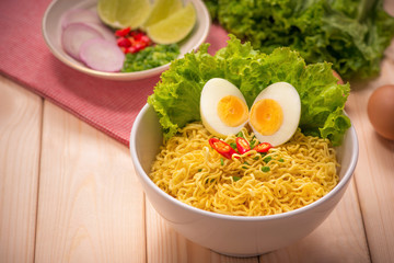 Instant noodles in bowl with vegetables and  boiled egg on wood background
