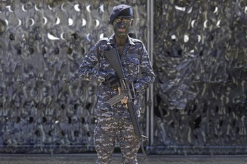 conceptual young soldier face with jungle camouflage paint and automatic rifles in hands