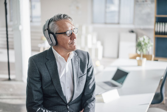 Senior businessman listening to music with headphones in office
