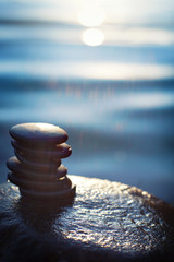 Stones for spa procedures lie on a pile on a wet boulder against a background of blue water,...