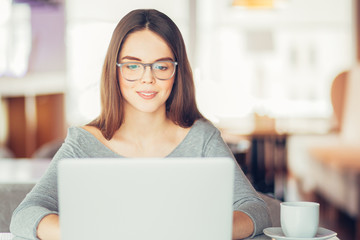 Smiling teenage girl sitting at laptop in cafe