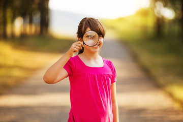 Beautiful little girl looking through  magnifying glass
 in the nature.