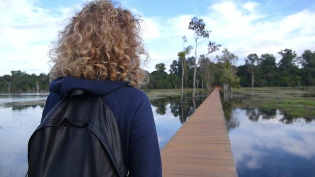 Blonde Woman With Backpack Walking To Forest On Bridge At Lake. Slow Motion. HD, 1920x1080.  