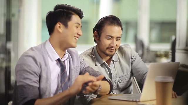 two asian entrepreneur discussing business in office using laptop computer.