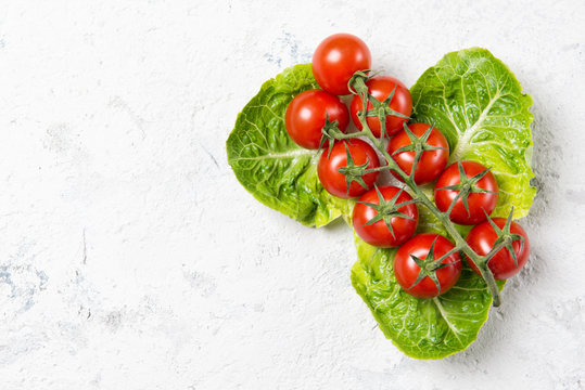 Ripe red cherry tomatoes on Romain Lettuce leaves, stone table, top view with copy space