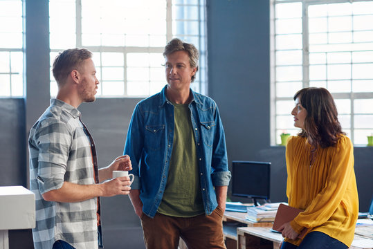 Three Collegues Standing In A Modern Office Talking Together