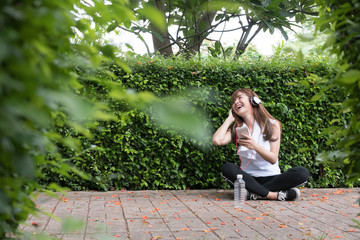 Naklejka premium asian woman with headphones. young female holding mobile smart phone. a girl listening to music in public park