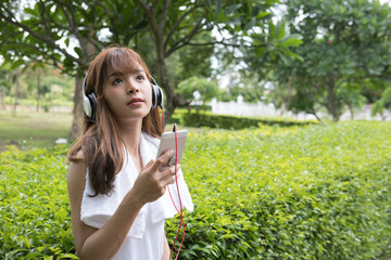 asian woman with headphones. young female  holding mobile smart phone. a girl listening to music in public park