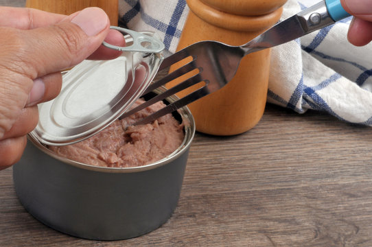 Fourchette piqu&eacute;e dans une bo&icirc;te de conserve de thon que l'on ouvre 