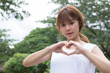 young woman making a heart gesture with her fingers. asian girl showing her love with hand sign in the park