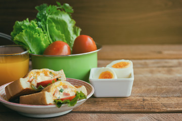 Pocket sandwich for breakfast or lunch. Homemade sandwich with hard boiled eggs and mayonnaise decorated by lettuce and tomato. Baked sandwich on lovely plate serve with orange juice on wood table.