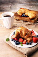 Delicious breakfast with fresh croissants, coffee and ripe berries on old wooden background