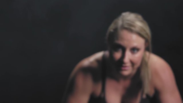 Focusing zoom shot of a sitting athletic caucasian woman smiling at the camera on a foggy dark background