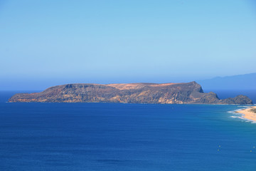 Fototapeta na wymiar Ilheu da Cal barren uninhabitated island to the south of Ponta Da Calheta, Porto Santo with Madeira to the right on the horizon