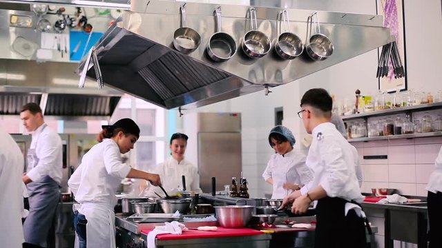 Workers bustling in the kitchen. The workers working on the kitchen. The man take a saucepan, the girl mix the dish on the stove.