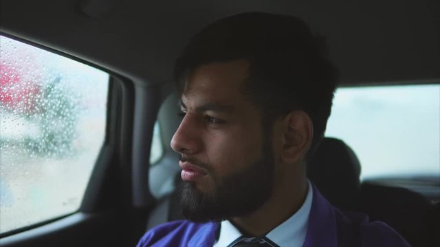 Young muslim businessman riding in the car on passenger's seat. Rain outside the car. Passenger in taxi