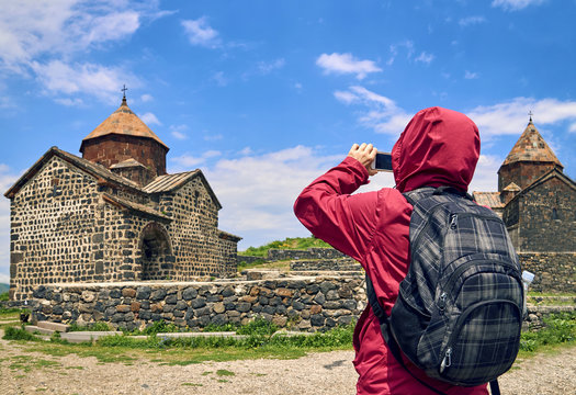 Female tourist taking photo of ancient monastery in Armenia using smart phone