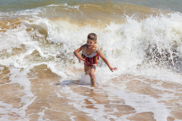 Little boy running in sea surf at the beach