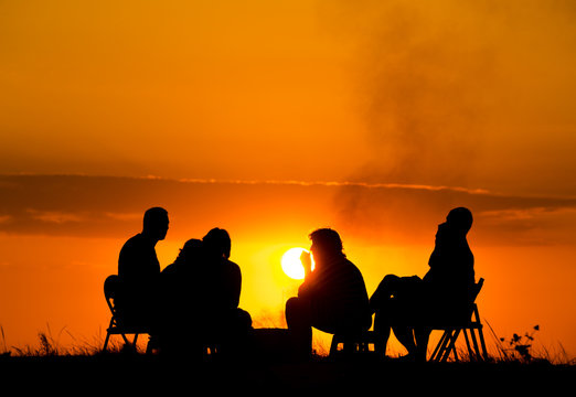group of people in camping sitting near campfire against sunset