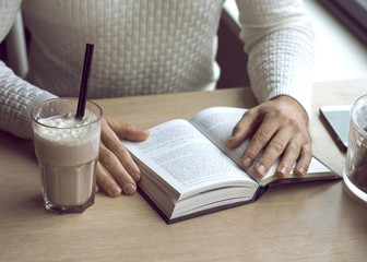 Young man reading book with cacao in cafe at autumn, cozy time and pastel colors