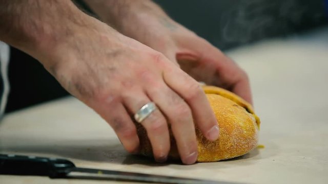 The cook cut the hot bread into a two pieces at the table. The man check for the raw loaf.