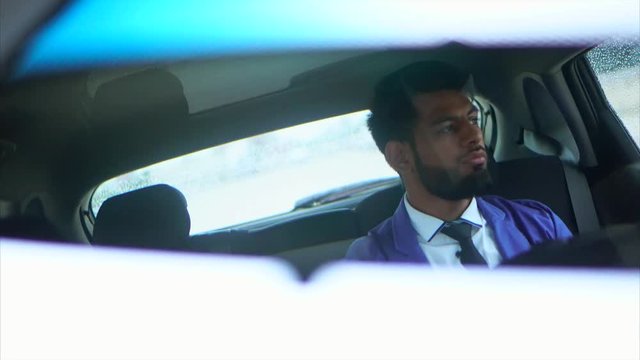 Reflection in the rearview mirror of the young muslim business man that sitting on the rear seat in the car