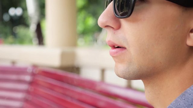 Close up portrait of young man in black sunglasses smoke electronic cigarette outdoor. Vaper. Steam.