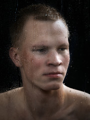 Portrait of a young man through the glass. The window in raindrops