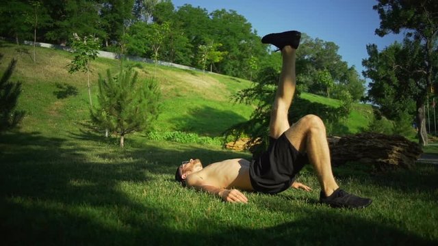 Strong man do one leg glute bridge exercises sunny green park rapid slow motion