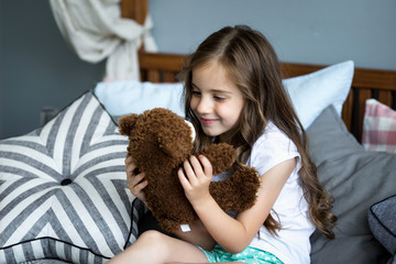Cute little girl is playing with a toy bear on the bed